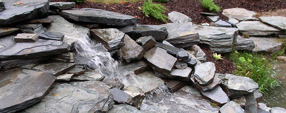 A slate waterfall with rocks and bushes in the background.