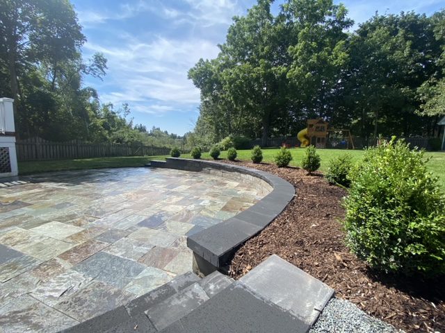 A backyard with a stone patio and landscaping.